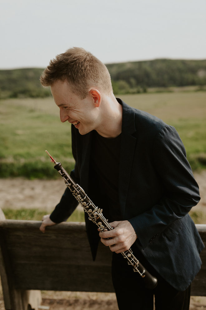 Aleh Remezau looking down at his oboe, outdoors in the countryside