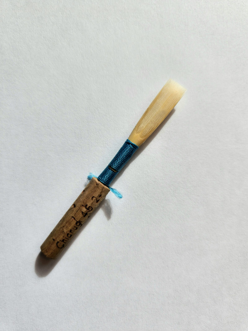 A finished oboe reed with blue thread on a white background